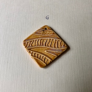 May include: A square ceramic tile with a brown and white wavy pattern. The tile has a hole in the top for hanging.