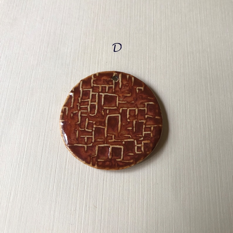 May include: A round ceramic ornament with a brown and white geometric pattern. The ornament has a hole at the top for hanging.