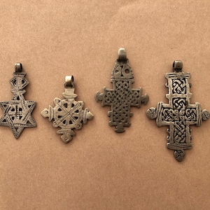 May include: Four silver-toned pendants with intricate designs. The pendants are in the shape of a star, a cross, and two different styles of crosses. The pendants are all on a brown background.