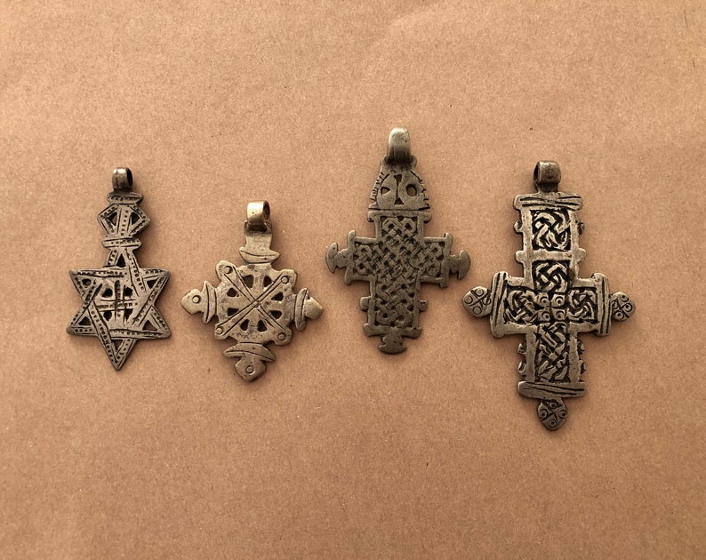 May include: Four silver-toned pendants with intricate designs. The pendants are in the shape of a star, a cross, and two different styles of crosses. The pendants are all on a brown background.