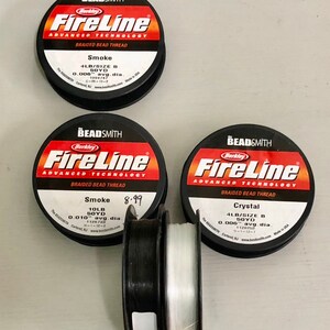 May include: Three spools of Berkley FireLine braided bead thread. The spools are labeled with the thread type, size, and color. The colors are Smoke, Smoke, and Crystal. The thread is 4lb and 50 yards.