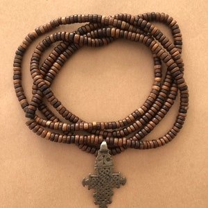 May include: A brown wooden beaded necklace with a silver cross pendant. The necklace is made of multiple strands of beads and is approximately 40 inches long.