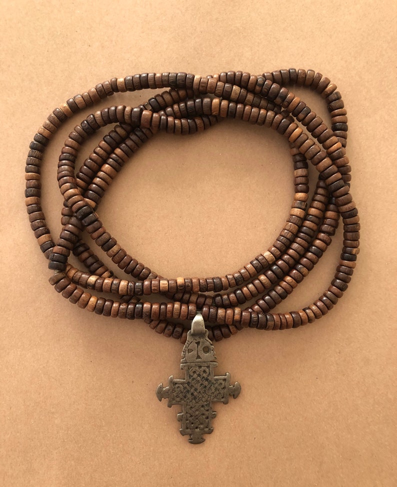 May include: A brown wooden beaded necklace with a silver cross pendant. The necklace is made of multiple strands of beads and is approximately 40 inches long.