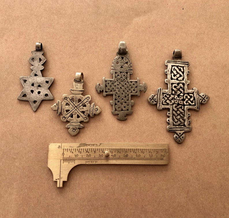 May include: Four silver pendants, including a star of David and three crosses, are displayed on a brown surface. A ruler is included for scale.