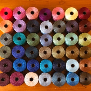 May include: Assortment of 36 spools of embroidery floss in various colours, including red, blue, green, yellow, and purple. The spools are arranged in a grid pattern on a wooden surface.