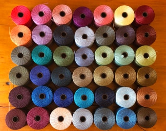 以下が含まれることがあります： 赤、青、緑、黄、紫など、さまざまな色の刺繍糸の糸巻き36個の詰め合わせ。糸巻きは木製の表面にグリッド状に配置されています。