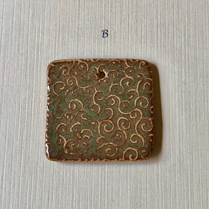 May include: A square ceramic tile with a green and brown glaze. The tile has a decorative pattern of swirls and is edged with a brown border. The tile has a small hole in the center.