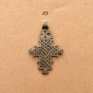 May include: A silver-toned cross pendant with intricate designs. The cross is made of metal and has a loop at the top for hanging.
