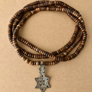 May include: A brown wooden beaded necklace with a silver pendant featuring a six-pointed star design.