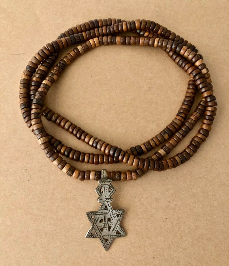 May include: A brown wooden beaded necklace with a silver pendant featuring a six-pointed star design.
