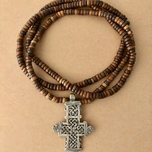 May include: A brown wooden beaded necklace with a silver cross pendant. The cross has a detailed, intricate design.