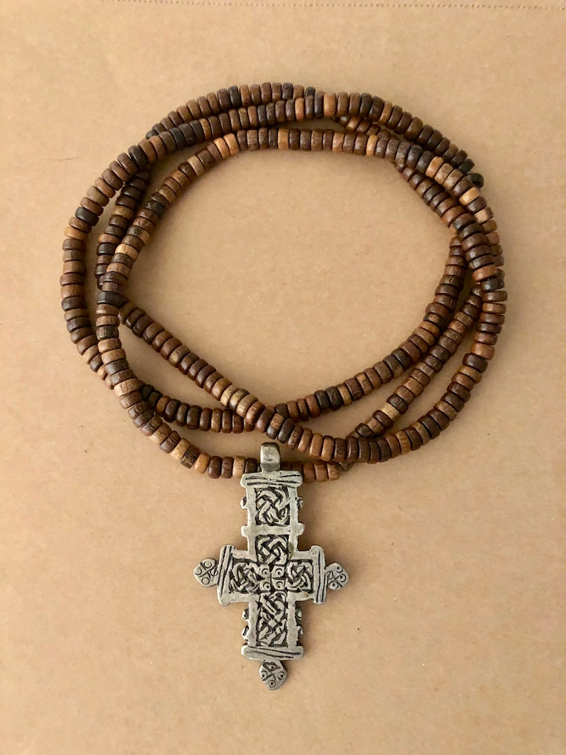 May include: A brown wooden beaded necklace with a silver cross pendant. The cross has a detailed, intricate design.