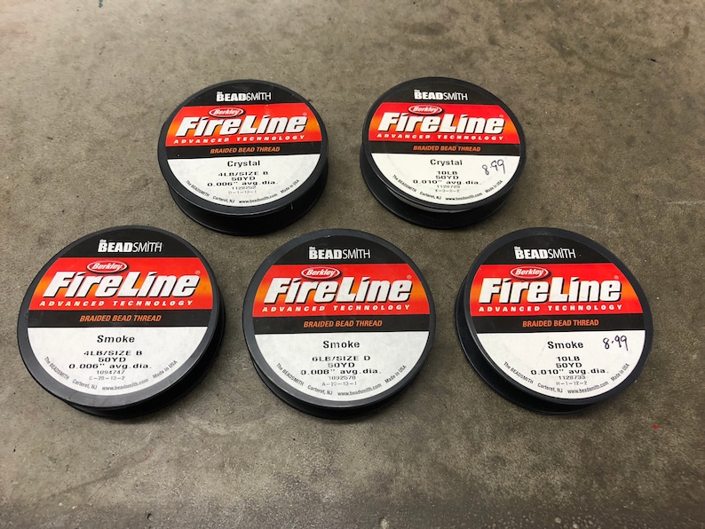 May include: Five spools of Berkley FireLine braided bead thread. The spools are black with red and white text. The spools are labeled with different sizes and colors of thread, including Crystal, Smoke, and 4LB/Size B. The price of one spool is $8.99.
