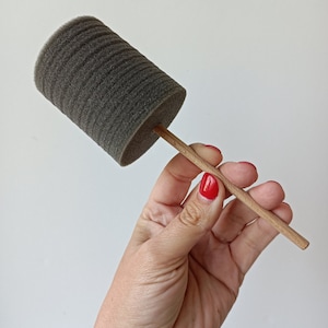 Könnte beinhalten: Eine graue Schaumstoffrolle mit einem Holzgriff. Die Rolle wird in einer Hand mit rotem Nagellack gehalten.