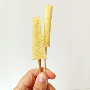 May include: Two yellow sponges on wooden sticks. The sponges are different sizes and shapes.