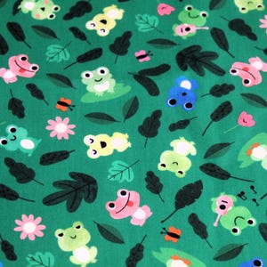 May include: Green fabric with a repeating pattern of frogs, butterflies, leaves, and flowers. The frogs are in various colours, including green, blue, pink, and yellow.