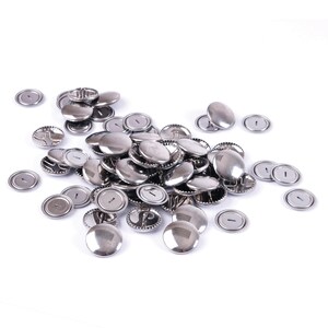 May include: A large collection of circular, silver-coloured metal button blanks. Each piece features a smooth, reflective domed front surface and a flat back with a small, centred horizontal slot for attachment, arranged in a loose pile.