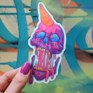 May include: A sticker of a purple skull with a pink ice cream cone on top. The ice cream is dripping down the skull's face. The sticker is on a blue and orange background.