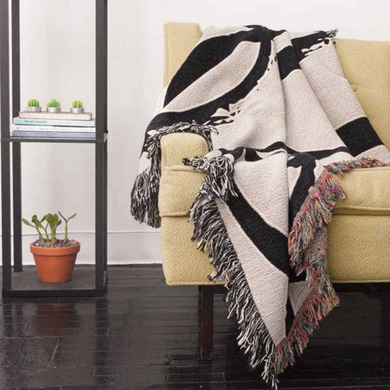 May include: A black and white woven throw blanket with a fringe border. The blanket is draped over a yellow armchair.