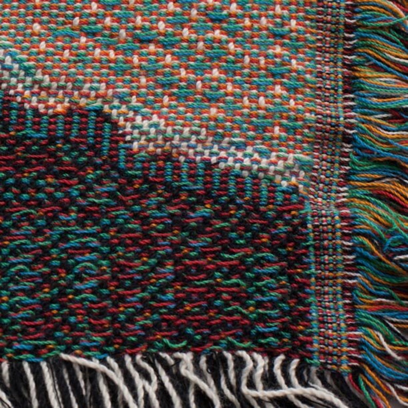 May include: A woven throw blanket with a colorful geometric pattern and fringe on all sides. The blanket is made of a soft, textured fabric and features a variety of colors, including red, blue, green, and black.