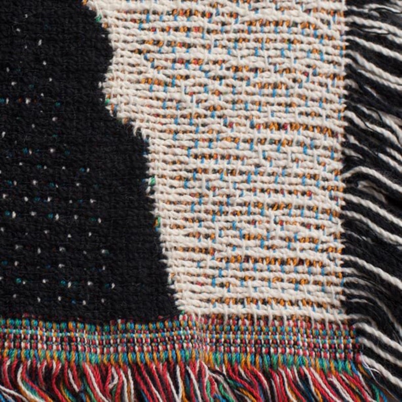 May include: A woven throw blanket with a black and white geometric pattern. The blanket has a fringe border with red, blue, green, and yellow threads.