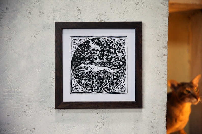 May include: Black and white woodblock print of a dog running through a forest scene. The print is framed in a dark wood frame.