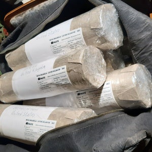 May include: A black bag filled with several brown paper-wrapped packages. Each package has a white label with the text "United States" and "United Kingdom" and a "PASTS" logo.