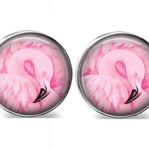 May include: A pair of round, silver-toned earrings. Each earring features a pink flamingo illustration with a black beak and a soft, feathery appearance. The flamingo is set against a pink background.