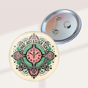 May include: A round button with a clock design. The button features a cream background with a central clock face in pink and green, surrounded by decorative elements. The text "WAIT JUST A CLOCK TICK" is printed around the clock face.