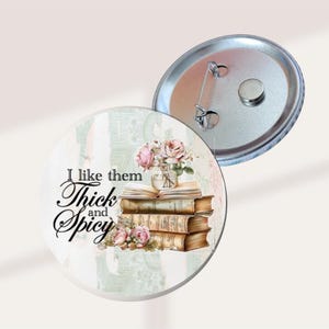 May include: A round button with the text "I like them Thick and Spicy" in black script. The button features a stack of old books with a vase of pink roses. The back of the button is silver with a pin.