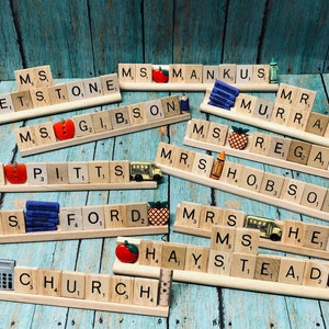 May include: A collection of wooden letter tiles spelling out teacher names, including "Ms. Stone", "Ms. Gibson", "Mr. Murray", "Ms. Regan", "Mrs. Hobson", "Mrs. Ford", "Mrs. Heun", "Ms. Haystead", and "Mr. Church". Each name is decorated with small school-themed embellishments, such as apples, pencils, and a school bus.