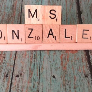 May include: A wooden name sign with the name "GONZALEZ" spelled out in Scrabble tiles. The tiles are arranged on a wooden base with a mermaid figurine on the left and a cartoon fish and lobster figurine on the right.