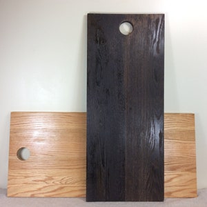 May include: Two wooden cutting boards, one stained dark brown and one natural wood color. Both boards have a round hole in the top.