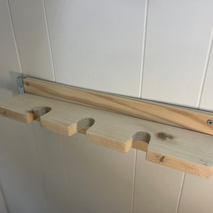 May include: Wooden wall-mounted shelf with four cutouts for holding items. The shelf is made of light wood and has a metal bracket on the right side. The numbers 1, 2, 3, and 4 are written on the shelf.