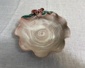 May include: A small, scalloped ceramic dish with a swirl pattern in shades of brown and white. The dish has a green leaf and three pink flower accents.