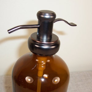 May include: A brown glass bottle with a black and copper pump dispenser. The bottle has a textured surface and is designed for dispensing liquids.