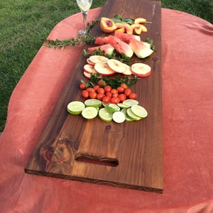 May include: A long, rectangular wooden serving board with a handle. The board is filled with sliced fruit, including watermelon, peaches, apples, and limes. There are also small red tomatoes on the board.