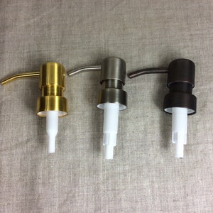 May include: Three soap dispensers with different finishes: gold, silver, and bronze. Each dispenser has a white plastic pump and a curved spout.