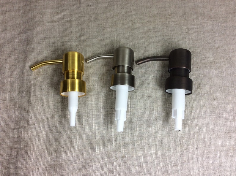 May include: Three soap dispensers with different finishes: gold, silver, and bronze. Each dispenser has a white plastic pump and a curved spout.