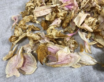 May include: A pile of dried flower petals in shades of pink and brown. The petals are scattered on a light gray fabric surface.