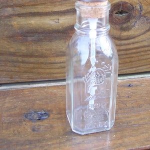 K&ouml;nnte beinhalten: Eine klare Glasflasche mit einem Korkverschluss. Die Flasche ist mit den Worten "Eight Ounces Pure Honey" gepr&auml;gt.