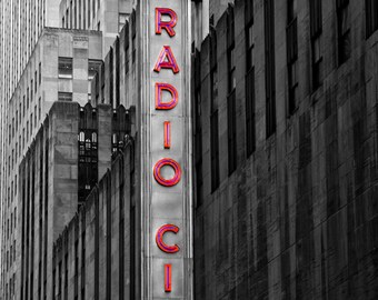May include: A black and white photo of a building with a large red neon sign that says "RADIO CITY MUSIC HALL".
