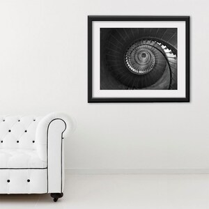 May include: Black and white photograph of a spiral staircase framed in a black frame. The photo is hanging on a white wall.