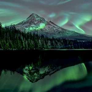 May include: A mountain peak with snow-capped summit reflected in a still lake. The sky is filled with vibrant green aurora borealis.