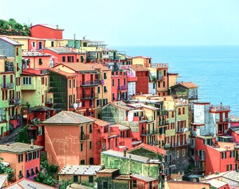 May include: A colorful hillside village with houses stacked on top of each other, overlooking a blue ocean. The houses are painted in shades of red, orange, yellow, and green.
