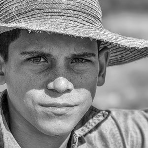 May include: A black and white portrait of a person wearing a straw hat with a wide brim. The person is also wearing a collared shirt. The image is a close-up, focusing on the person's face and the texture of the hat.