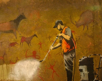 May include: A person in a safety vest and a hard hat uses a pressure washer to clean a cave wall with prehistoric cave paintings of animals and humans. The cave paintings are in red, brown, and black.