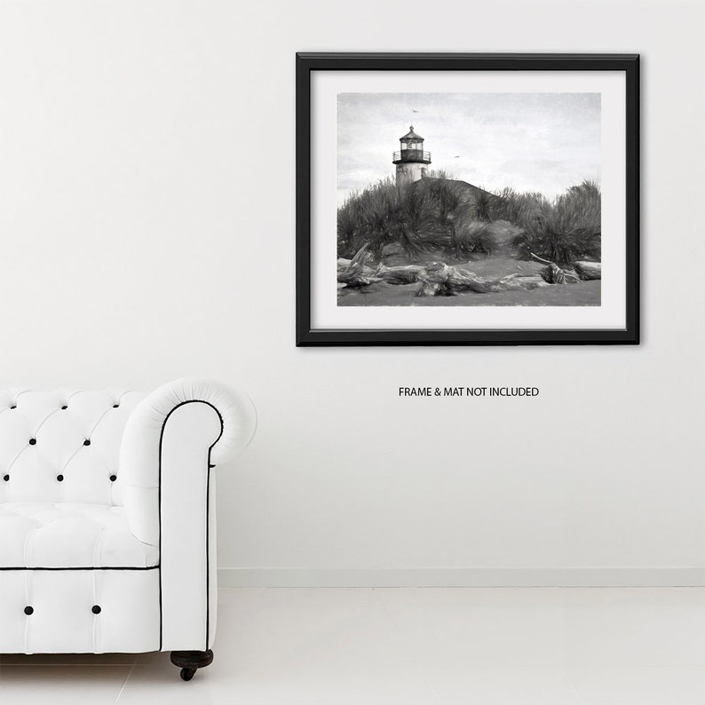 May include: Black and white photograph of a lighthouse on a sandy beach with driftwood in the foreground. The lighthouse is tall and white with a black roof and a black and white striped tower. The beach is sandy and the water is calm.