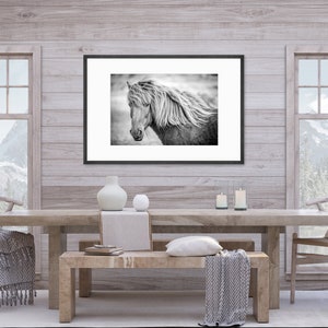 May include: A black and white photograph of a horse with a long flowing mane, framed in a black frame and hanging on a light wood wall. The photo is above a wooden table with two chairs and a bench.
