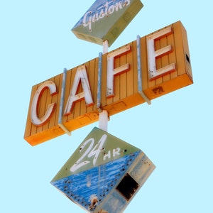 May include: An aged, weathered cafe sign with the word "CAFE" in large, white, illuminated letters. Above, a sign reads "Gaston's" and below, a sign indicates "24 HR". The sign is painted in shades of yellow, green, and blue against a light blue sky.